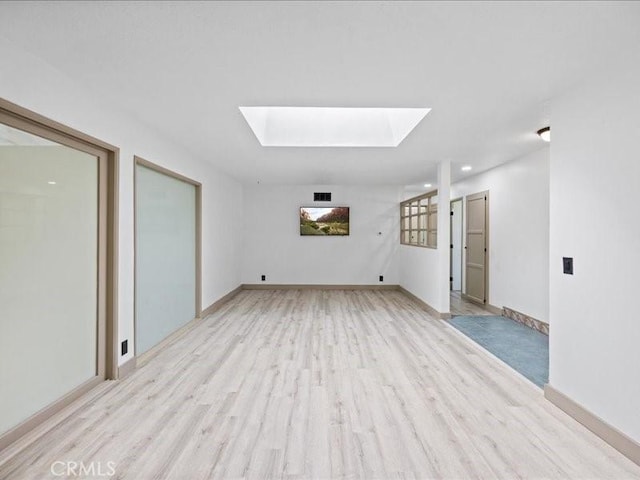 unfurnished room featuring light wood-type flooring, a skylight, visible vents, and baseboards