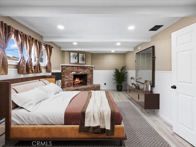 bedroom featuring a fireplace, wood finished floors, visible vents, wainscoting, and beam ceiling