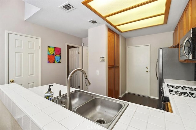 kitchen featuring tile counters, brown cabinetry, stainless steel microwave, and a sink