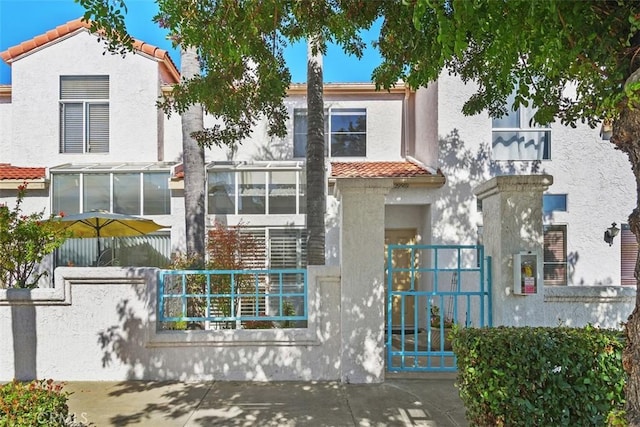 view of front facade with a fenced front yard, a tiled roof, a gate, and stucco siding