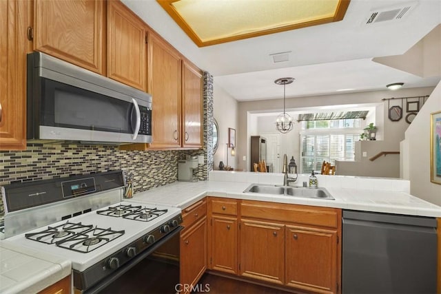 kitchen with a peninsula, a sink, visible vents, appliances with stainless steel finishes, and tasteful backsplash