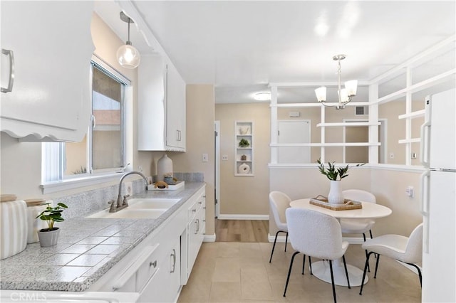 kitchen featuring hanging light fixtures, an inviting chandelier, freestanding refrigerator, white cabinetry, and a sink