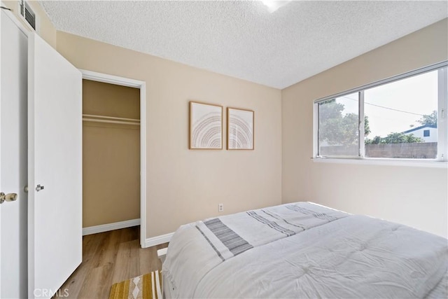 bedroom featuring a textured ceiling, visible vents, baseboards, a closet, and light wood-type flooring