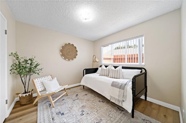 bedroom with a textured ceiling, baseboards, and wood finished floors