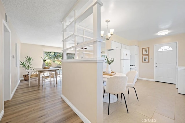 dining space with a textured ceiling, light wood-type flooring, a chandelier, and baseboards