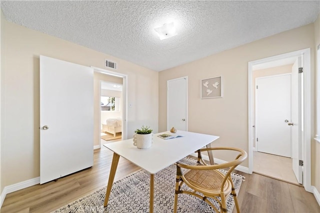 home office featuring baseboards, light wood-style flooring, visible vents, and a textured ceiling