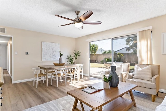 living area with light wood-type flooring, ceiling fan, baseboards, and a textured ceiling