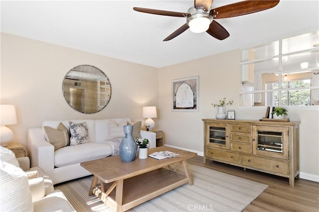 living area featuring a ceiling fan, baseboards, and wood finished floors