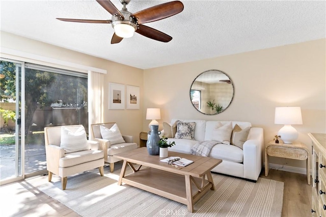 living area with a textured ceiling, baseboards, a ceiling fan, and light wood-style floors