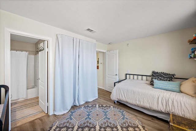 bedroom with ensuite bath, visible vents, and wood finished floors