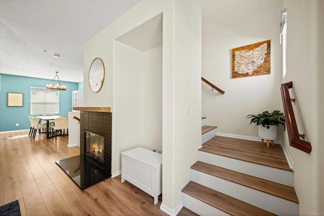 stairs featuring baseboards, a chandelier, wood finished floors, and a glass covered fireplace