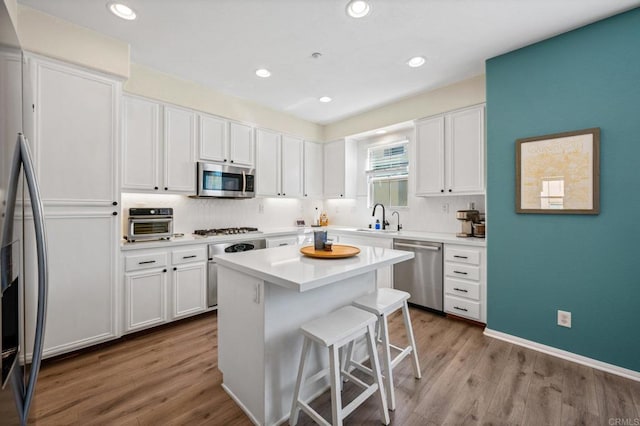 kitchen featuring stainless steel appliances, white cabinetry, a sink, wood finished floors, and a kitchen breakfast bar