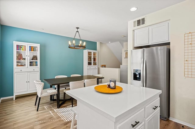 kitchen with a kitchen island, visible vents, light wood-style floors, white cabinets, and stainless steel fridge