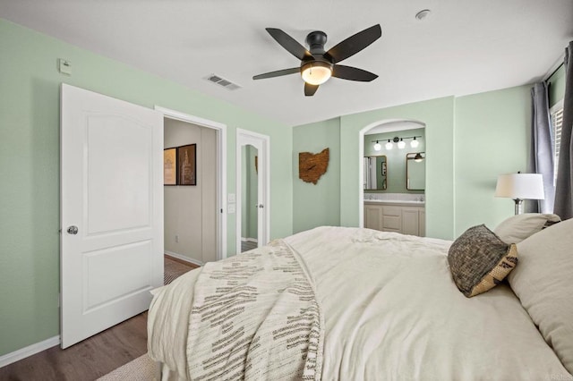 bedroom with arched walkways, visible vents, connected bathroom, wood finished floors, and baseboards