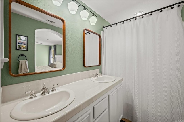 full bathroom featuring double vanity, visible vents, a sink, and a textured wall