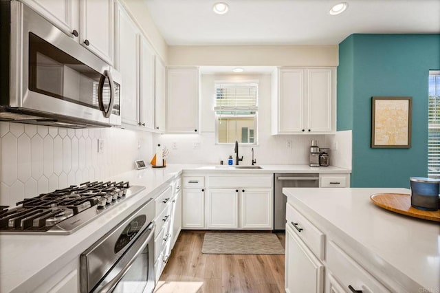 kitchen featuring stainless steel appliances, light countertops, light wood-type flooring, white cabinetry, and a sink