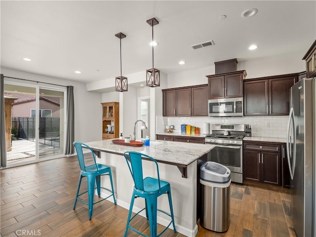 kitchen featuring light stone counters, stainless steel appliances, visible vents, dark wood-type flooring, and a sink