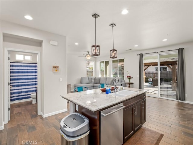 kitchen with a sink, dark wood-style floors, hanging light fixtures, dishwasher, and a center island with sink