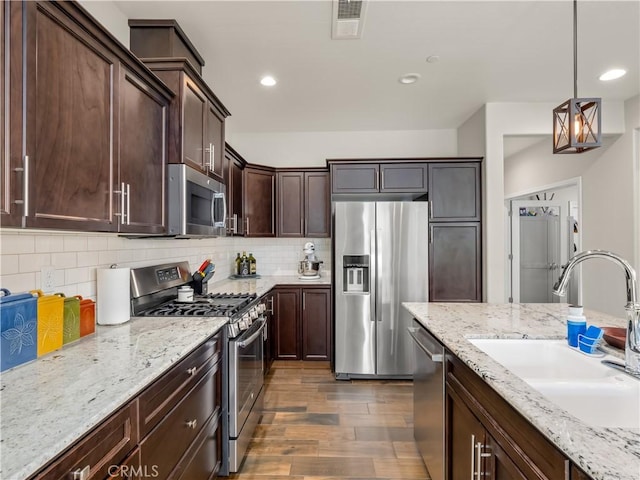 kitchen featuring light stone counters, decorative backsplash, appliances with stainless steel finishes, a sink, and dark brown cabinets