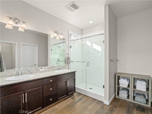 bathroom with wood finish floors, visible vents, a sink, and a shower stall