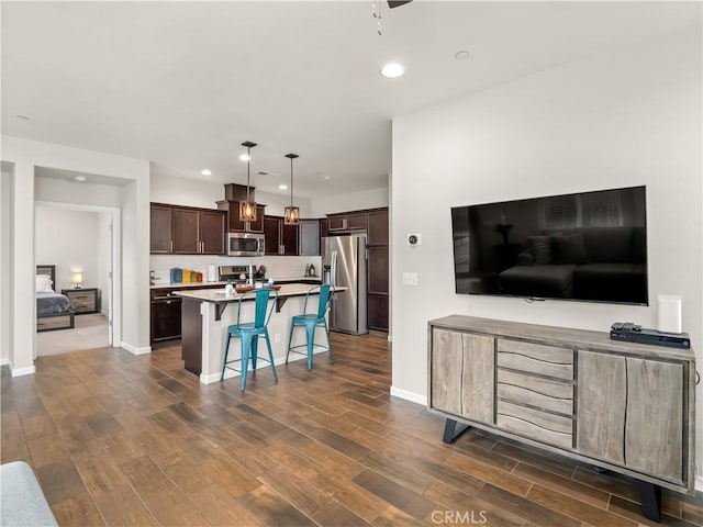 kitchen with dark wood-style floors, dark brown cabinets, appliances with stainless steel finishes, and a breakfast bar area