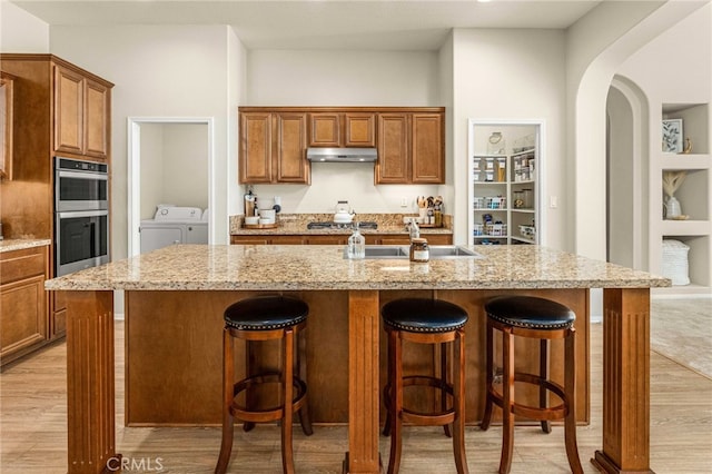 kitchen featuring appliances with stainless steel finishes, washing machine and dryer, light wood-style floors, and under cabinet range hood