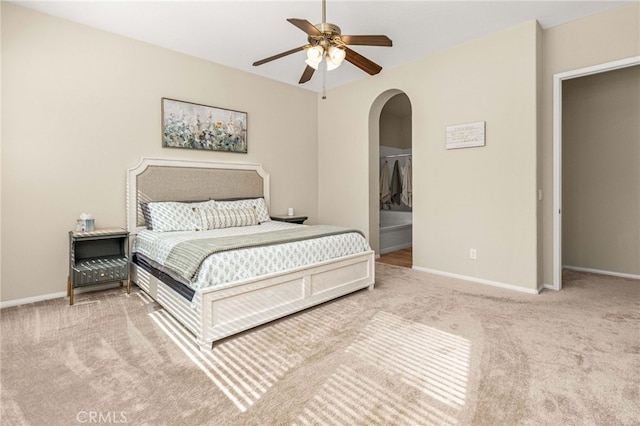 carpeted bedroom with a ceiling fan, arched walkways, and baseboards