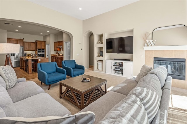 living area featuring arched walkways, a fireplace, visible vents, baseboards, and built in features