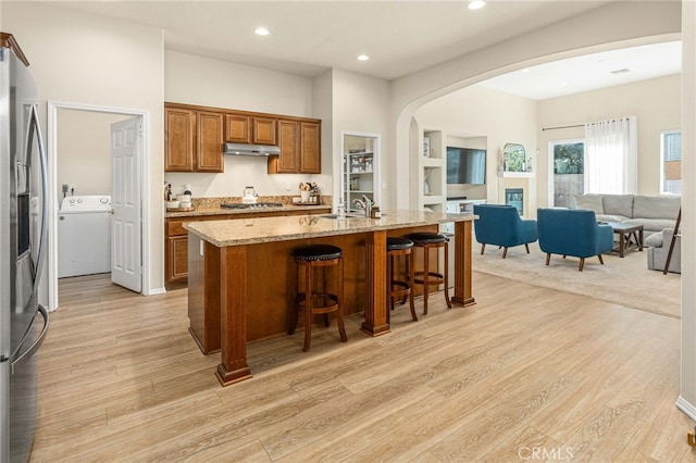 kitchen featuring arched walkways, under cabinet range hood, a kitchen breakfast bar, appliances with stainless steel finishes, and washer / dryer