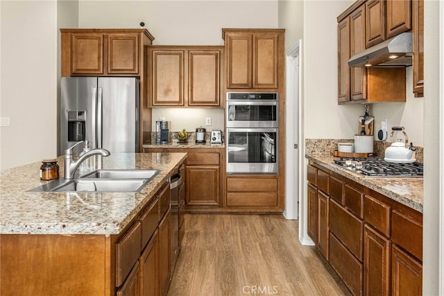 kitchen with under cabinet range hood, appliances with stainless steel finishes, brown cabinetry, and a sink