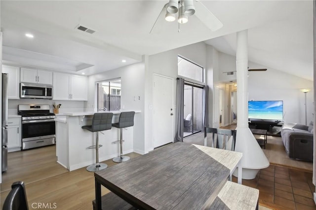 kitchen with a breakfast bar, stainless steel appliances, light countertops, visible vents, and a ceiling fan