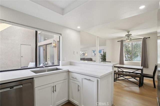 kitchen featuring a peninsula, light countertops, light wood-type flooring, stainless steel dishwasher, and a sink