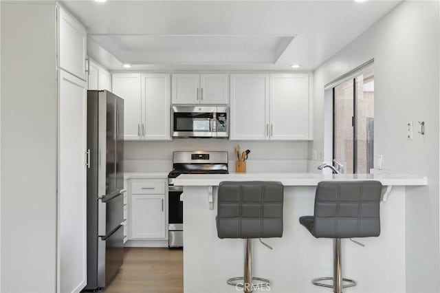 kitchen featuring stainless steel appliances, a peninsula, a kitchen bar, and white cabinetry