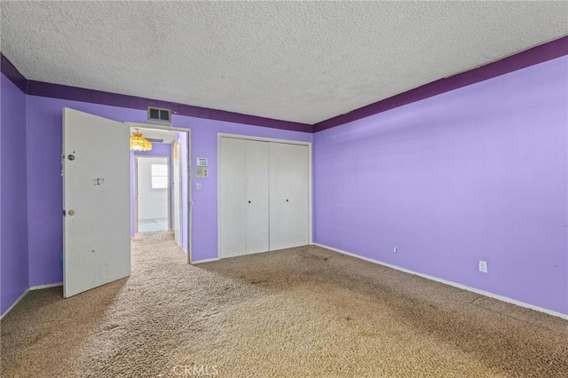 unfurnished bedroom with a textured ceiling, a closet, carpet, and visible vents