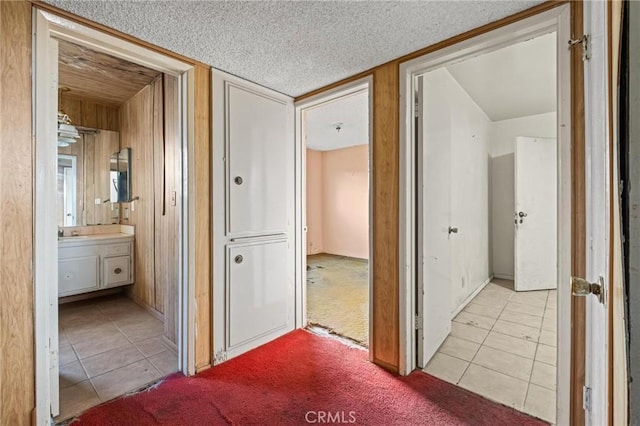 hallway with light tile patterned floors, light colored carpet, wood walls, a sink, and a textured ceiling