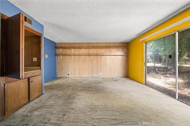 unfurnished living room with carpet, wooden walls, visible vents, and a textured ceiling