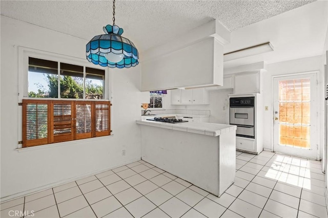 kitchen featuring a warming drawer, tile counters, white cabinets, stainless steel oven, and a peninsula