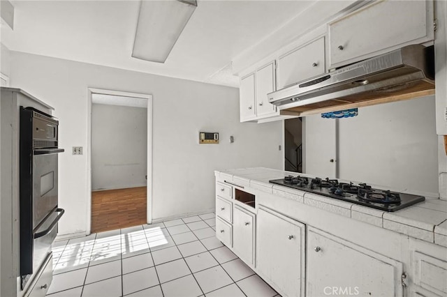 kitchen featuring tile countertops, light tile patterned flooring, white cabinets, black gas stovetop, and under cabinet range hood