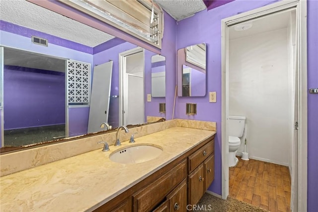 bathroom featuring a textured ceiling, toilet, wood finished floors, vanity, and visible vents