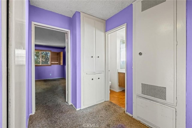 corridor featuring carpet floors, baseboards, and a textured ceiling