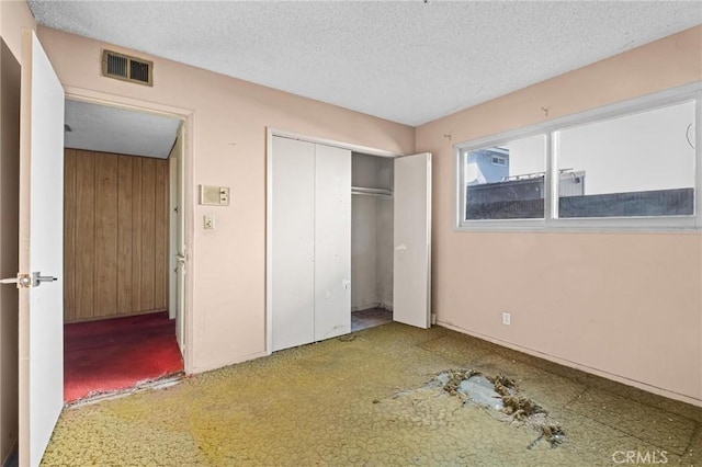 unfurnished bedroom featuring wooden walls, a closet, visible vents, and a textured ceiling