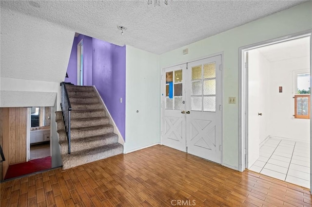 foyer entrance featuring a textured ceiling, french doors, stairway, and wood finished floors