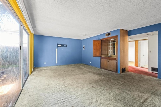 unfurnished living room with a textured ceiling, visible vents, and carpet flooring