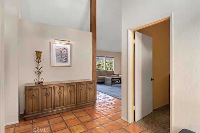 corridor with light carpet, baseboards, vaulted ceiling, and light tile patterned flooring