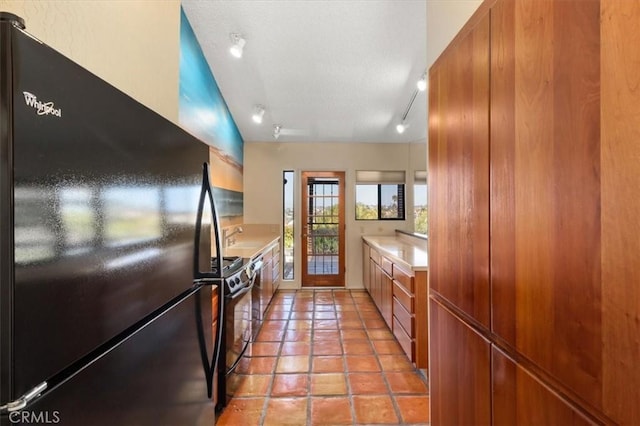 kitchen with range with gas stovetop, light tile patterned floors, light countertops, brown cabinetry, and freestanding refrigerator