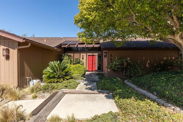 property entrance featuring roof with shingles and roof mounted solar panels