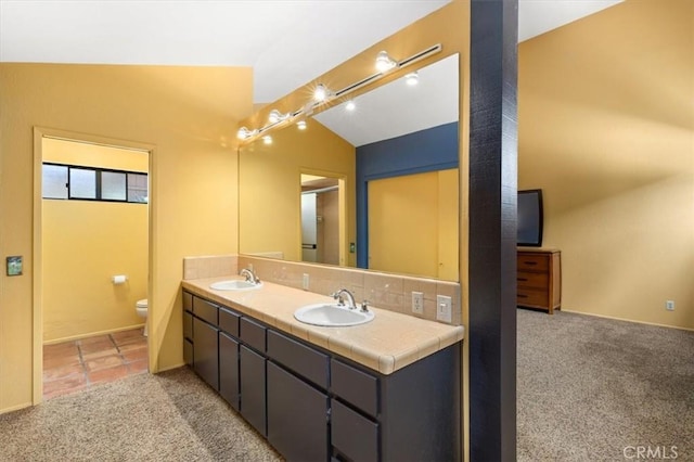 bathroom with vaulted ceiling, a sink, toilet, and double vanity