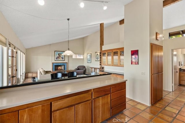 kitchen featuring open floor plan, a lit fireplace, light countertops, brown cabinetry, and pendant lighting