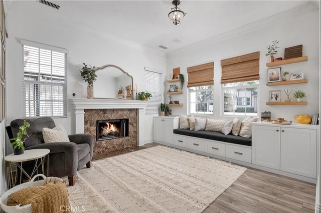 sitting room featuring ornamental molding, light wood-type flooring, visible vents, and a premium fireplace