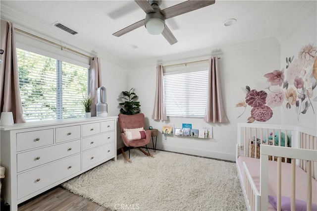 bedroom featuring a crib, baseboards, visible vents, ornamental molding, and wood finished floors